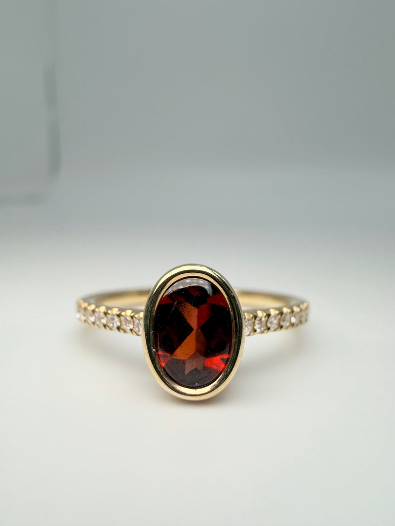 14Kt Yellow Gold .86Ct Oval Bezel Set Garnet Center With 1/10Tw Diamond On The Band (25330606)